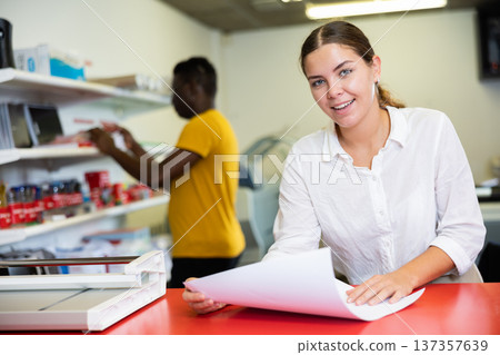 Attentive young female specialist verifying printed sheet during work in the print shop 137357639