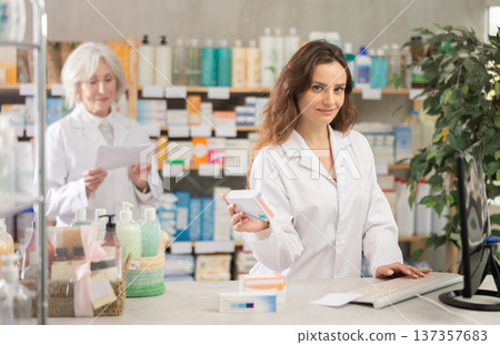 Female pharmacist using computer, companion at background Female pharmacist using computer, companion at background 137357683