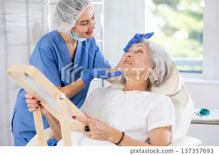 Mature patient with mirror, doctor with gloves Mature patient with mirror, doctor with gloves 137357693