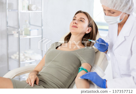 Female doctor doing injection to smiling calm young woman in clinic. 137357712