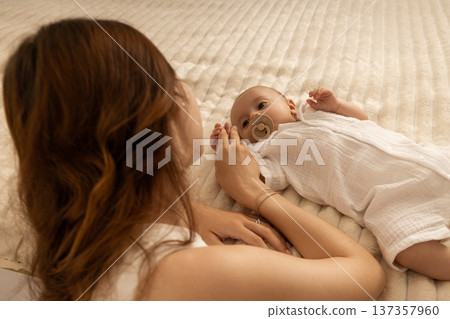 A mother interacts lovingly with her newborn on a soft blanket 137357960