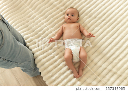 A baby lies on a soft blanket while being observed by a parent 137357965