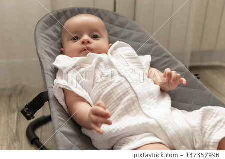 Cute baby relaxes in a comfortable bouncer at home Cute baby relaxes in a comfortable bouncer at home 137357996