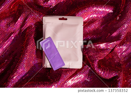 Face mask sachet and small packet on glittering pink sequin background. 137358352
