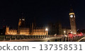 Elizabeth Tower and the Palace of Westminster illuminated at night beside a city road. A red double decker bus travels along the bridge under street lighting. 137358531