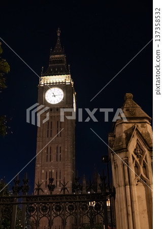 Close up Big Ben clock tower illuminated against a dark night sky. The iconic structure represents London travel and destination imagery. Close up Big Ben clock tower illuminated against a dark night sky. The iconic structure represents London travel and destination imagery. 137358532