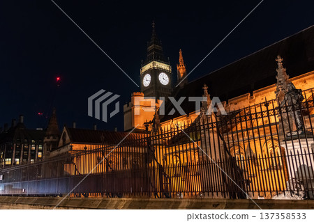 Big Ben clock tower seen from behind iron fencing at night. The layered view adds depth to London city landmark imagery. Big Ben clock tower seen from behind iron fencing at night. The layered view adds depth to London city landmark imagery. 137358533