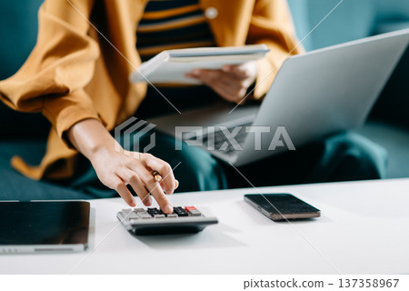 Women counting coins on calculator taking from the piggy bank. hand holding pen working on calculator to calculate on desk about cost at office. 137358967