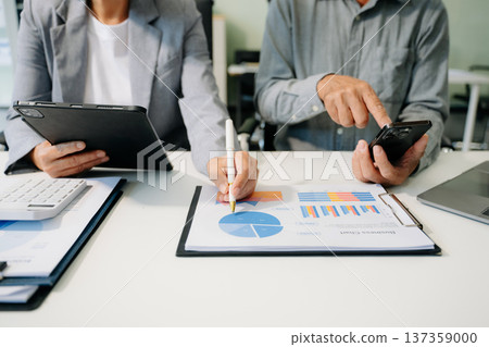 Business documents on office table with smart phone and laptop and two colleagues discussing data Business documents on office table with smart phone and laptop and two colleagues discussing data 137359000