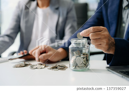 saving money with hand putting coins in jug glass and calculator to calculate budget concept saving money with hand putting coins in jug glass and calculator to calculate budget concept 137359027