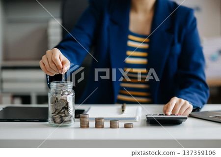 businesswoman holding coins putting in glass with using smartphone and calculator to calculate concept saving money for finance accounting in office 137359106
