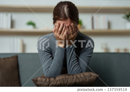 Emotional Distress. Woman covering her face in despair while sitting on a couch. Emotional Distress. Woman covering her face in despair while sitting on a couch. 137359519