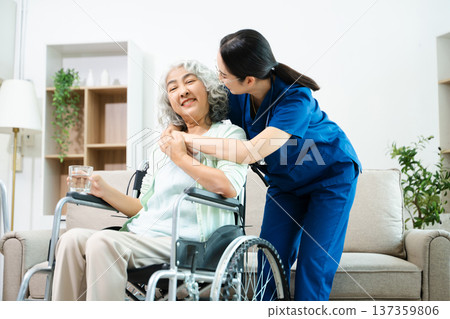 Asian nurse caring for smiling elderly woman in wheelchair at home. Senior care, home healthcare, nursing support, compassion, caregiver service concept Asian nurse caring for smiling elderly woman in wheelchair at home. Senior care, home healthcare, nursing support, compassion, caregiver service concept 137359806