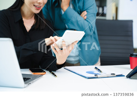 Asian businesswomen celebrating success in modern office. Teamwork, leadership, mentoring and collaboration concept with laptop and tablet. 137359836