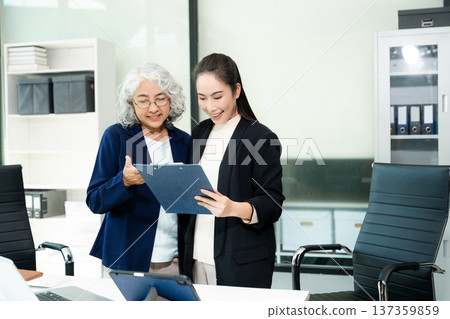 Senior and junior Asian businesswomen discussing documents in modern office, mentorship, teamwork, leadership Senior and junior Asian businesswomen discussing documents in modern office, mentorship, teamwork, leadership 137359859
