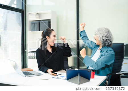 Senior and junior Asian businesswomen discussing documents in modern office, mentorship, teamwork, leadership 137359872