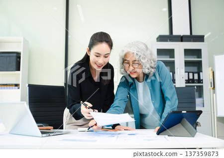 Senior and junior Asian businesswomen discussing documents in modern office, mentorship, teamwork, leadership 137359873