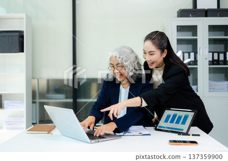 Asian business women discussing finance data using tablet and calculator in a modern office, showing teamwork, mentorship, analysis, and professional corporate collaboration. 137359900