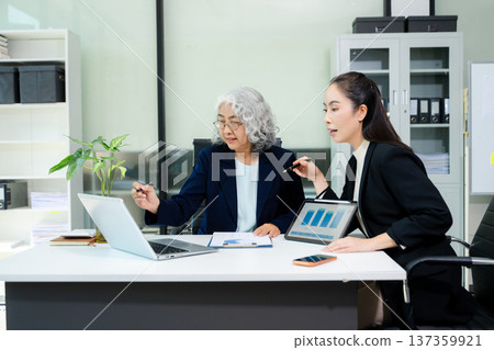 The scene highlights asian business professionals reviewing data and reports together, showing teamwork, mentorship, and strategic planning The scene highlights asian business professionals reviewing data and reports together, showing teamwork, mentorship, and strategic planning 137359921