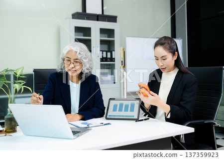 The scene highlights asian business professionals reviewing data and reports together, showing teamwork, mentorship, and strategic planning 137359923