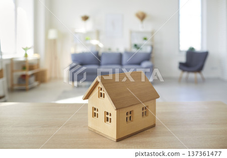 Closeup of little wooden toy house standing on table with empty living room in background Closeup of little wooden toy house standing on table with empty living room in background 137361477