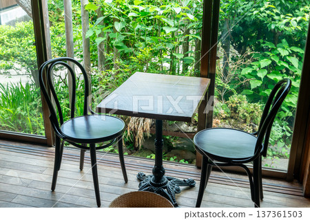 Wooden table and chairs by the window in a traditional Japanese cafe. Veranda seating overlooking the garden. Wooden table and chairs by the window in a traditional Japanese cafe. Veranda seating overlooking the garden. 137361503