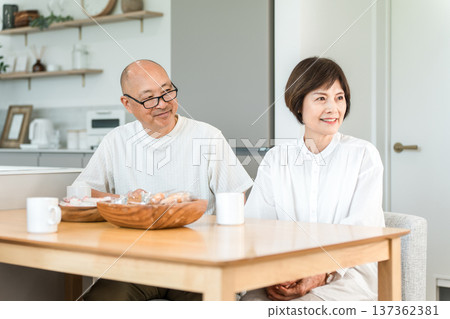 一對面帶著微笑的老年夫婦一邊喝咖啡一邊與家人交談。 一對面帶著微笑的老年夫婦一邊喝咖啡一邊與家人交談。 137362381