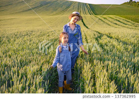 A woman and a young girl walk through a golden wheat field under a clear sky, enjoying a sunny day outdoors A woman and a young girl walk through a golden wheat field under a clear sky, enjoying a sunny day outdoors 137362995
