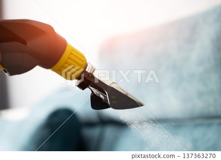 Cleaning nozzle of wet vacuum cleaner sprays water solution on upholstery fabric of sofa during professional deep cleaning service 137363270