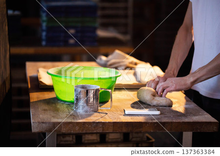 Professional baker hands kneading raw dough on wooden table for fresh bread preparation in bakery kitchen, artisanal food production Professional baker hands kneading raw dough on wooden table for fresh bread preparation in bakery kitchen, artisanal food production 137363384