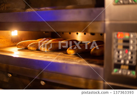Golden brown bread baking in commercial bakery oven, light illuminating fresh baked goods inside industrial kitchen equipment, close up view of warm fresh loaves Golden brown bread baking in commercial bakery oven, light illuminating fresh baked goods inside industrial kitchen equipment, close up view of warm fresh loaves 137363393