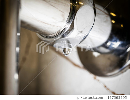 Water drop forming and falling from polished chrome towel warmer surface in modern bathroom, close-up view of plumbing leak and mineral deposits showing maintenance issue, urgent household repair Water drop forming and falling from polished chrome towel warmer surface in modern bathroom, close-up view of plumbing leak and mineral deposits showing maintenance issue, urgent household repair 137363395