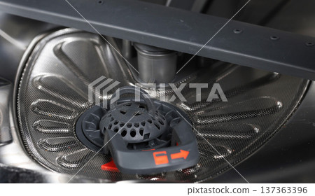 Close up view of dirty dishwasher filter system showing mesh surface and removable plastic component at bottom of appliance interior for maintenance 137363396