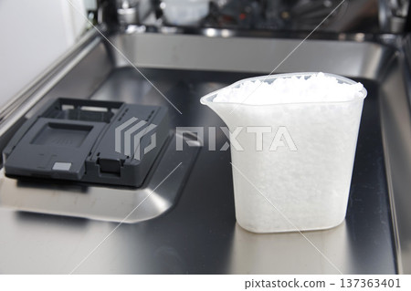 Dishwasher salt granules in measuring cup inside dishwasher for effective dish cleaning appliance maintenance hard water softening Dishwasher salt granules in measuring cup inside dishwasher for effective dish cleaning appliance maintenance hard water softening 137363401