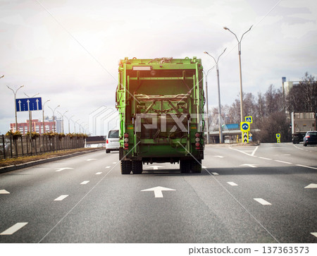 Green garbage truck driving on multi-lane highway, urban road infrastructure, waste transportation vehicle, city logistics, environmental service on street network. Copy space for text 137363573