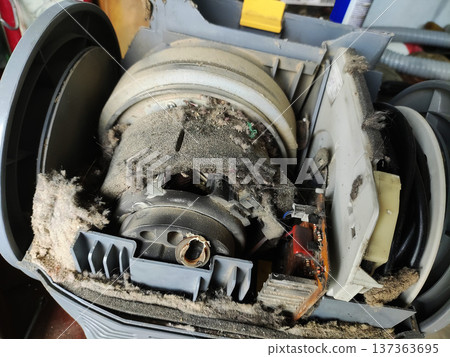 Internal view of dirty vacuum cleaner motor housing and components, revealing extreme dust and lint accumulation requiring maintenance or repair Internal view of dirty vacuum cleaner motor housing and components, revealing extreme dust and lint accumulation requiring maintenance or repair 137363695