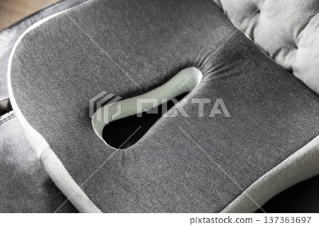 Ergonomic design of orthopedic seat cushion in gray fabric with central cutout for comfort and posture support on chair surface Ergonomic design of orthopedic seat cushion in gray fabric with central cutout for comfort and posture support on chair surface 137363697