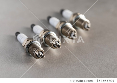 Automotive spark plugs arranged on grey background. Four new engine ignition components for internal combustion engine repair or maintenance. Automotive spark plugs arranged on grey background. Four new engine ignition components for internal combustion engine repair or maintenance. 137363705