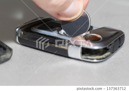Hand removing flat circular battery from electronic car key remote control housing for replacement operation close up indoors view on neutral background 137363712