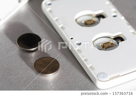 Replacement of coin cell batteries for electronic device, close up view of open back casing with power cells next to internal circuit, detail of modern tech repair on textured gray surface 137363716