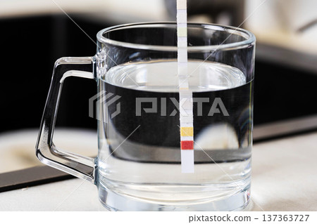 Water quality testing in clear glass mug with immersion of chemical indicator strip revealing color change for analysis of liquid parameters and evaluation of water composition 137363727