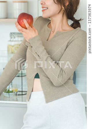 Woman eating an apple in the kitchen (diet, vegetarian) Woman eating an apple in the kitchen (diet, vegetarian) 137363974
