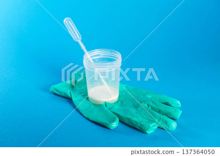 A container with prostate fluid and ejaculate stands on a medical glove against a blue background. Conceptual study of protozoan infection and decreased hormones and libido. Prostatitis and 137364050
