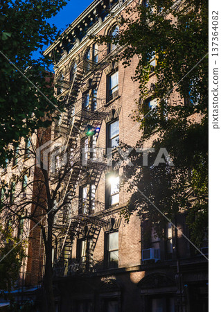 Historic New York residential building facade with fire escapes and sunlight through trees 137364082
