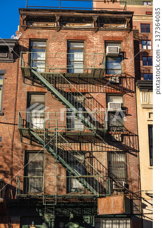 Classic New York brick apartment facade with metal fire escape stairs 137364085