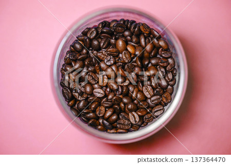 Roasted coffee beans in a glass jar on a pink background top view. Minimalist composition of dark coffee beans in container over pink surface. 137364470