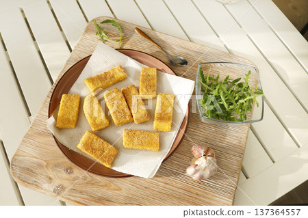Sliced pieces of fried hard polenta on plate on table. Cornmeal in kitchen. Ingredients and traditional Italian cuisine. Sliced pieces of fried hard polenta on plate on table. Cornmeal in kitchen. Ingredients and traditional Italian cuisine. 137364557