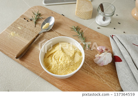 Corn flour in white ceramic bowl on wooden cutting board in kitchen. Parmesan and rosemary. Ingredients for polenta. Traditional Italian cuisine. 137364559