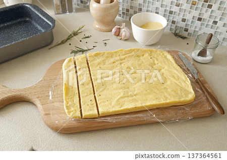 Anonymous person cut hard polenta into pieces with knife on table. Corn flour in the kitchen. Ingredients and traditional Italian cuisine. 137364561