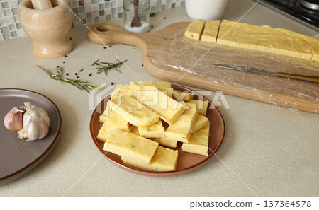 Sliced pieces of hard polenta on table. Cornmeal in kitchen. Ingredients and traditional Italian cuisine. 137364578